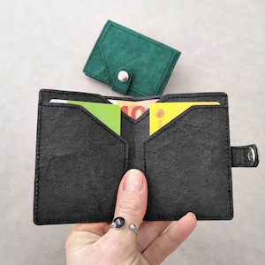 May include: A black leather wallet with multiple card slots and a flap closure. The wallet is open and has several cards inside. The wallet is sitting on a white surface.