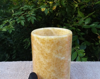 Puede incluir: Un recipiente cilíndrico de piedra natural de color amarillo con una superficie lisa y pulida. El recipiente tiene un aspecto ligeramente texturizado y moteado.