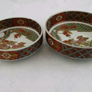 Puede incluir: Dos cuencos redondos de cerámica con fondo blanco y diseños florales intrincados en rojo, verde, dorado y negro. Los cuencos son de tamaños ligeramente diferentes.