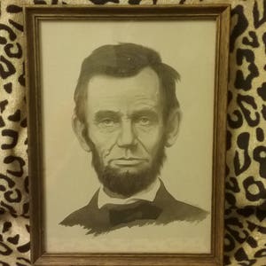 May include: A black and white portrait of a man with a beard and mustache. The man is wearing a dark suit and a white shirt with a bow tie. The portrait is framed in a wooden frame.