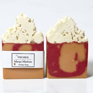 May include: Two bars of artisan soap with a swirl of red and orange colors. The soap is topped with a white swirl design and has a label that reads "PREMIER BATH & BODY CARE Mango Madness Artisan Soap".