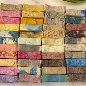 May include: A stack of 25 handmade soap bars in various colors and patterns. The soap bars are arranged in a rectangular shape and are all the same size. The soap bars are made with natural ingredients and are free of harsh chemicals.