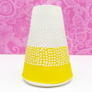 Pode incluir: Um vaso de cer&acirc;mica branco com um design de bolinhas amarelas e brancas. O vaso tem a forma de um cone e uma abertura larga na parte superior.