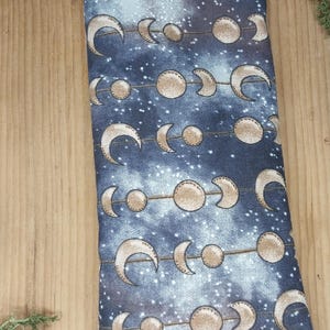May include: A blue fabric eye pillow with a moon phases pattern. The pillow is filled with flax seeds and lavender.