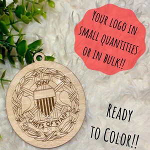 May include: A round, unfinished wooden ornament with the words "JOINT CHIEFS OF STAFF" engraved around a shield design. The text "YOUR LOGO IN SMALL QUANTITIES OR IN BULK!!" and "READY TO COLOR!!" are also visible.