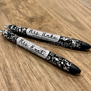 May include: Two black pens with silver glitter. The pens have labels that say "Composition Book" and include the teacher's name, "Mrs. Unke" and "Mrs. Hunt". The labels also say "100 Sheets 200 Pages".