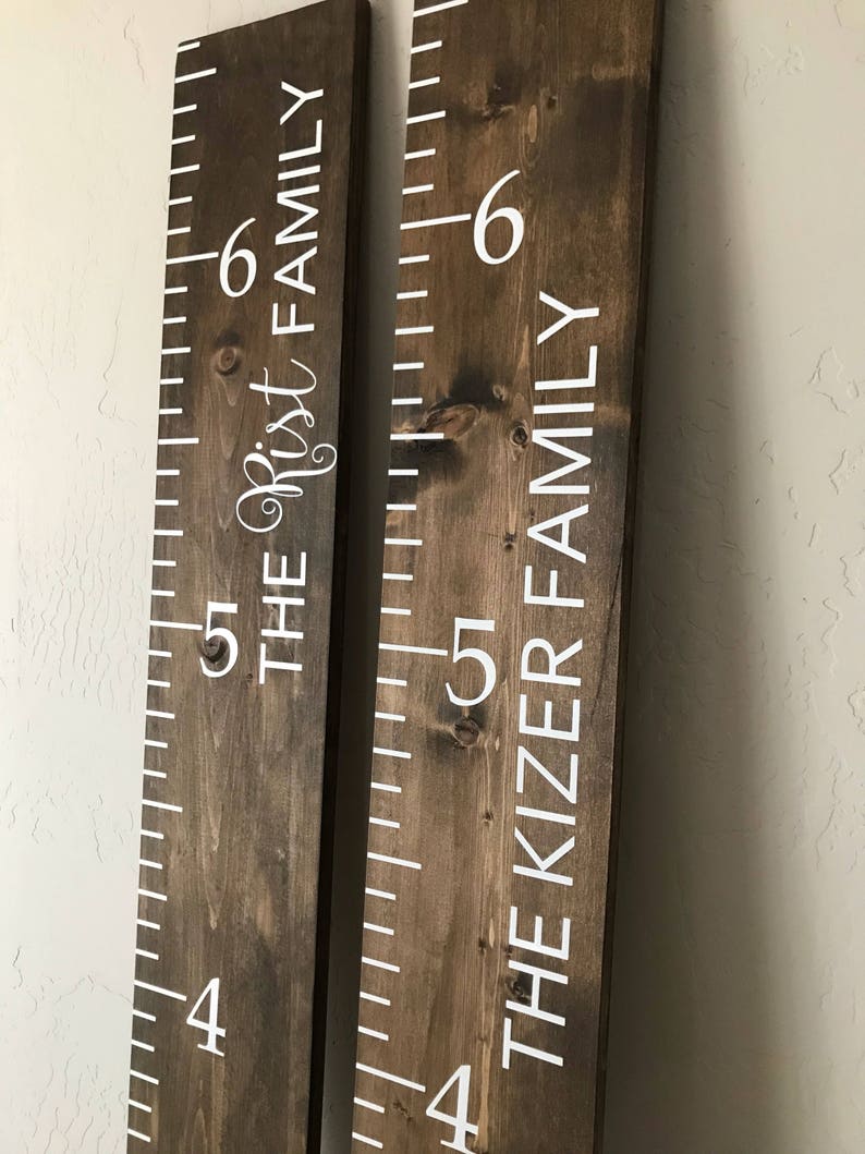 May include: Two brown wooden growth charts with white numbers and text. The left chart reads "The Rist Family" and the right chart reads "The Kizer Family".