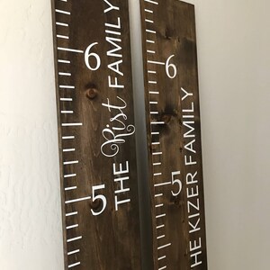 May include: Two brown wooden growth charts with white painted markings and numbers. The left chart says "The Rist Family" and the right chart says "The Kizer Family".