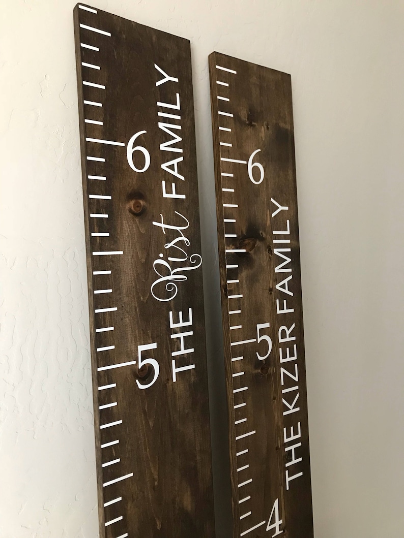 May include: Two brown wooden growth charts with white painted markings and numbers. The left chart says "The Rist Family" and the right chart says "The Kizer Family".