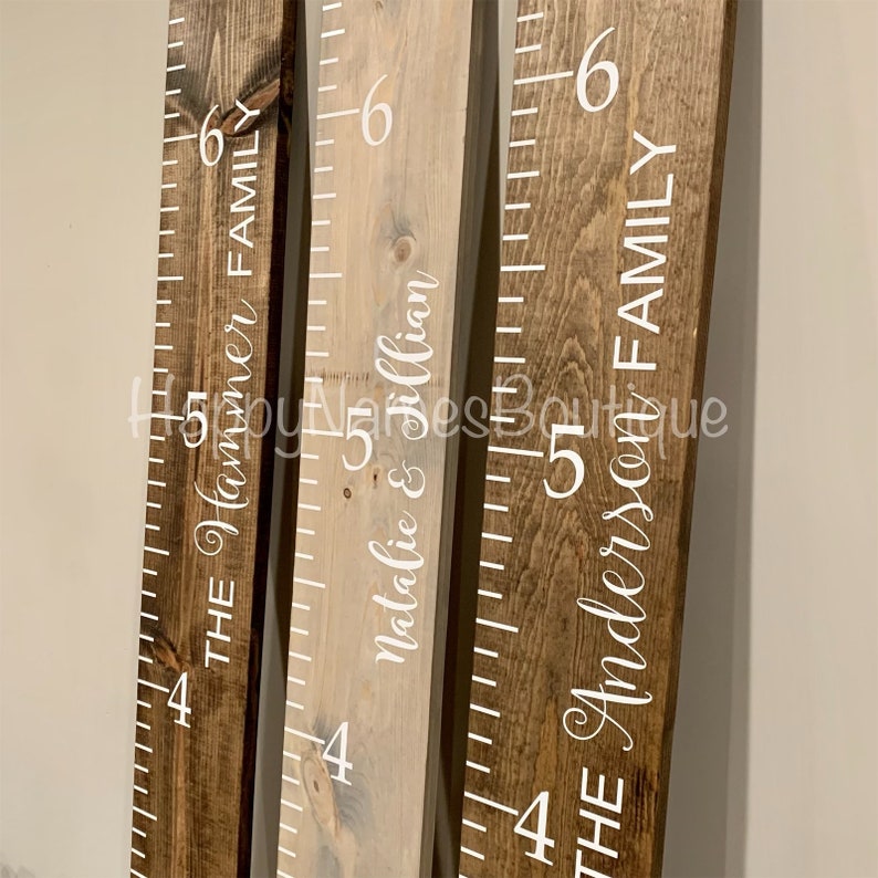 May include: Three wooden growth charts with white painted numbers and names. The charts are labelled "The Hammer Family", "Natalie & Jillian", and "The Anderson Family".