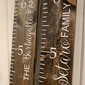 May include: Two wooden growth charts with white numbers and text. The left chart reads "The Barbagallo Family" and the right chart reads "The Dettore Family".