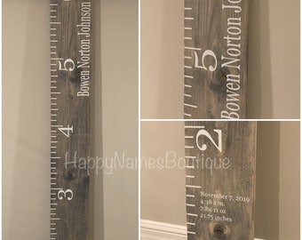 May include: A grey wooden growth chart with white markings and the name "Bowen Norton Johnson" printed on it. The chart includes measurements in inches and a date, time, weight, and length at birth.