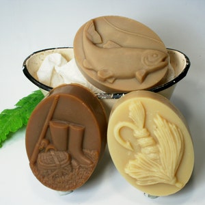 May include: Four oval-shaped soaps with different fishing-themed designs. One soap features a brown trout, another has a fishing boot and tackle box, and two soaps have a fly fishing lure.