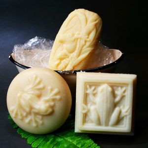 May include: Three white soap bars with frog designs. The soap bars are in a white and black bowl. The soap bars are on a black background.