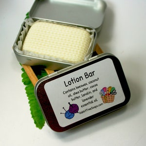 May include: A silver tin with a white lotion bar inside. The tin has a label that reads "Lotion Bar" and lists the ingredients: beeswax, coconut oil, shea butter, cocoa butter, lanolin, and lavender essential oil. The label also includes the website address: RabbitTreeSoaps.com.
