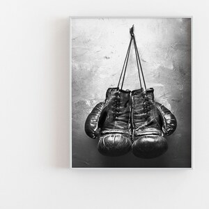 May include: A pair of black leather boxing gloves hanging on a hook against a textured gray wall.