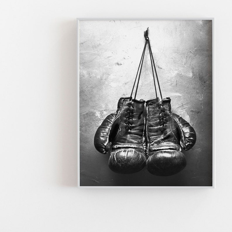 May include: A pair of black leather boxing gloves hanging on a hook against a textured gray wall.