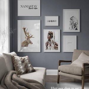 Pode incluir: Um interior de sala de estar com uma parede cinza e um sof&aacute; branco. A parede &eacute; decorada com impress&otilde;es emolduradas que mostram um veado, uma mulher com penas, uma fase lunar, uma coruja e o texto "NAMASTAY here now". H&aacute; um cobertor de l&atilde; marrom no sof&aacute; e uma poltrona marrom com uma almofada.