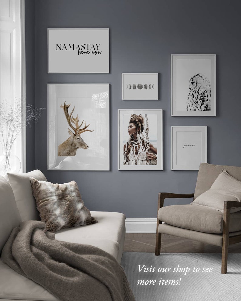 Pode incluir: Um interior de sala de estar com uma parede cinza e um sof&aacute; branco. A parede &eacute; decorada com impress&otilde;es emolduradas que mostram um veado, uma mulher com penas, uma fase lunar, uma coruja e o texto "NAMASTAY here now". H&aacute; um cobertor de l&atilde; marrom no sof&aacute; e uma poltrona marrom com uma almofada.