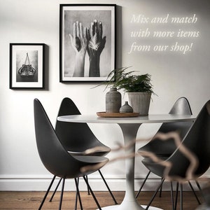 May include: A white round table with a black tulip base and four black chairs. The table is set with a wooden tray, two small gray vases, and a larger gray planter with a green plant. Two black and white framed prints hang on the wall behind the table. The text "Mix and match with more items from our shop!" is written on the wall.