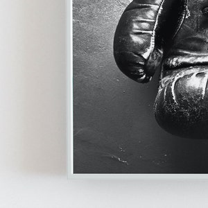 May include: A pair of black leather boxing gloves hanging on a wall. The gloves are worn and have a distressed look.
