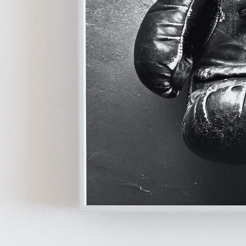 May include: A pair of black leather boxing gloves hanging on a wall. The gloves are worn and have a distressed look.