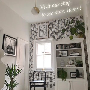 May include: A black and white geometric wallpaper pattern with a hexagonal design. The wallpaper is in a hallway with a white door, a black chair, and a white bookshelf with books and decorative items.