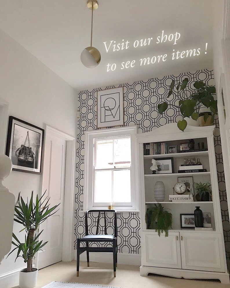 May include: A black and white geometric wallpaper pattern with a hexagonal design. The wallpaper is in a hallway with a white door, a black chair, and a white bookshelf with books and decorative items.