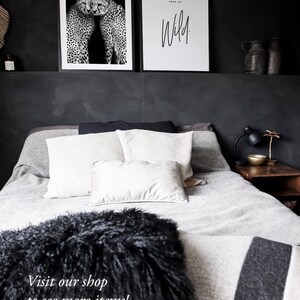 May include: Black and white photograph of two cheetahs cuddling. The image is framed and hanging on a black wall above a bed with white and gray bedding. The text "I'll keep you safe, you keep me wild." is printed on a white framed poster hanging next to the cheetah photo.
