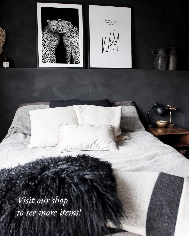 May include: Black and white photograph of two cheetahs cuddling. The image is framed and hanging on a black wall above a bed with white and gray bedding. The text "I'll keep you safe, you keep me wild." is printed on a white framed poster hanging next to the cheetah photo.