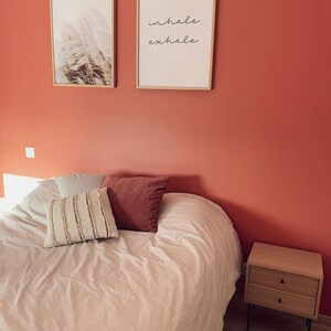 May include: A bedroom with a white bed, two framed prints on the wall, and a wooden nightstand. The print on the right says "inhale exhale".
