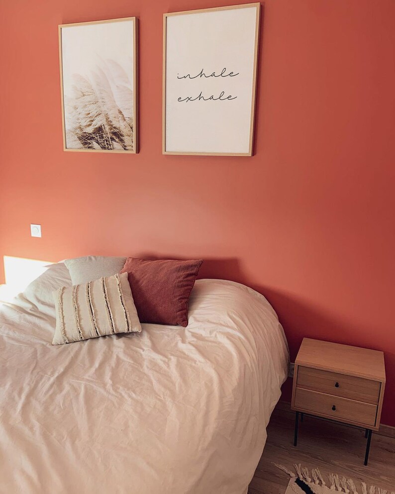 May include: A bedroom with a white bed, two framed prints on the wall, and a wooden nightstand. The print on the right says "inhale exhale".