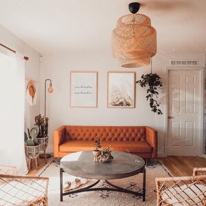 May include: A living room with a brown leather sofa, a round coffee table, and two wicker chairs. There are two framed prints on the wall, one with the words "inhale exhale" and the other with a nature scene. A hanging wicker light fixture hangs from the ceiling.