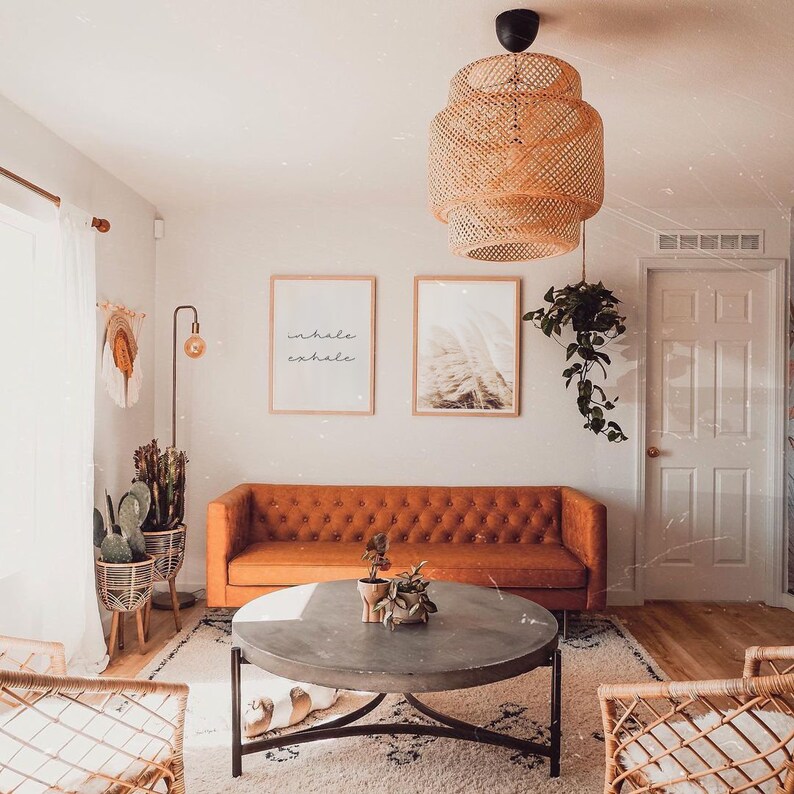 May include: A living room with a brown leather sofa, a round coffee table, and two wicker chairs. There are two framed prints on the wall, one with the words "inhale exhale" and the other with a nature scene. A hanging wicker light fixture hangs from the ceiling.