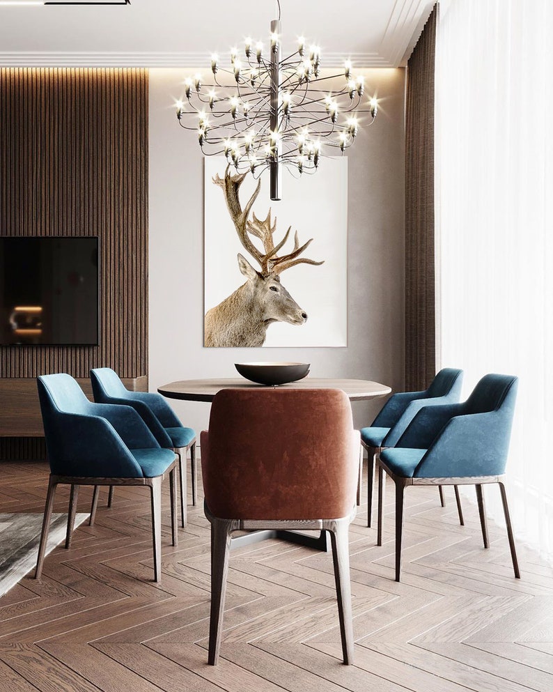 Pode incluir: Uma sala de jantar com uma mesa de madeira e seis cadeiras. A mesa &eacute; redonda e tem um tampo marrom. As cadeiras s&atilde;o estofadas em tecido azul e marrom. Um grande lustre pendura sobre a mesa. Uma impress&atilde;o emoldurada de uma cabe&ccedil;a de veado pendura na parede atr&aacute;s da mesa.