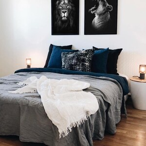 May include: A gray linen bed with a white throw blanket and two black and white framed pictures of lions above the headboard. The bed has a blue and black patterned throw pillow and a blue pillowcase.
