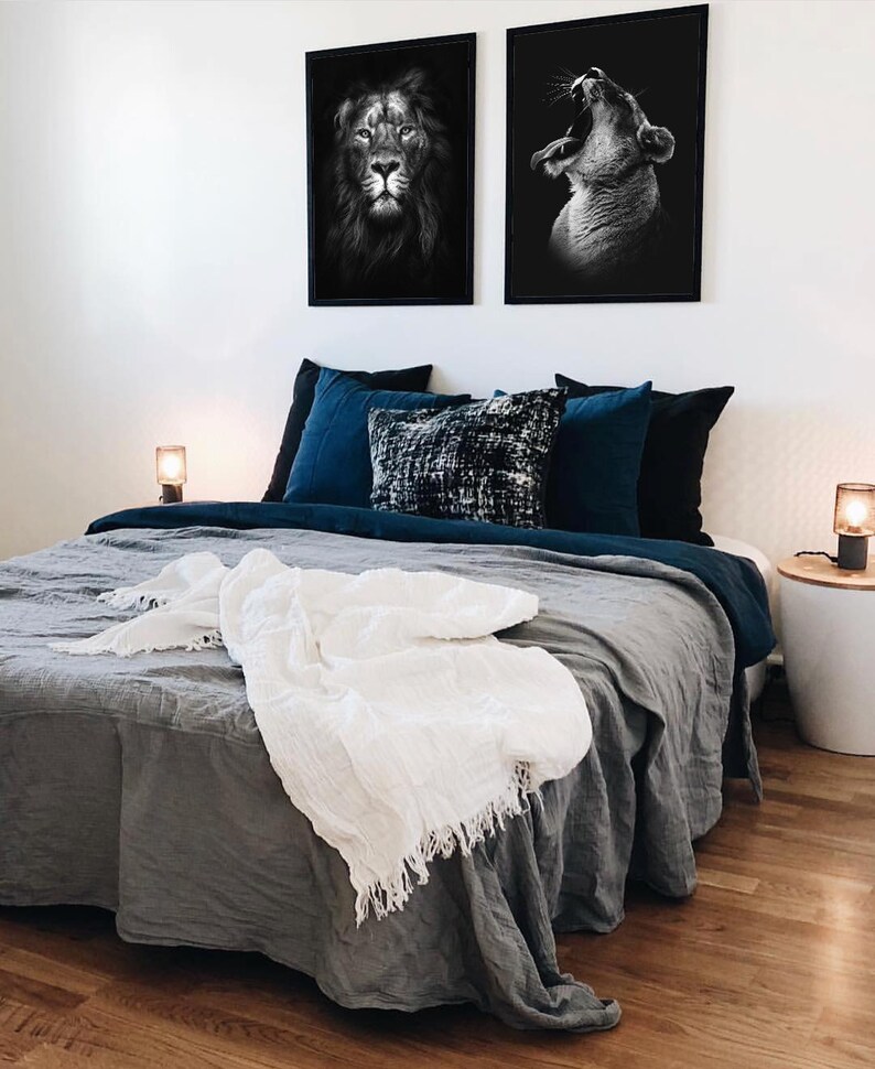 May include: A gray linen bed with a white throw blanket and two black and white framed pictures of lions above the headboard. The bed has a blue and black patterned throw pillow and a blue pillowcase.