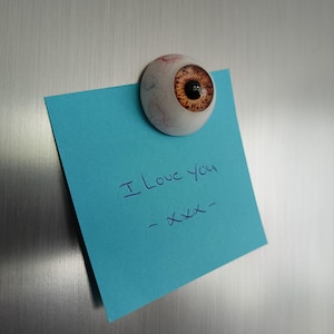 Könnte beinhalten: Ein blauer Haftnotiz mit dem Text "I love you - xxx" auf einer Edelstahlfläche mit einem Augen-Magneten.