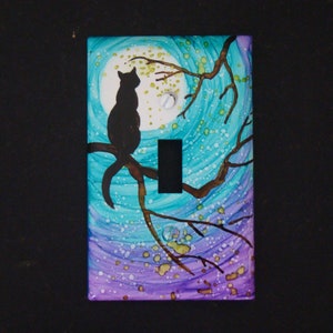 May include: A light switch cover with a hand-painted design featuring a black cat silhouette on a branch against a swirling blue and purple background with white and gold accents.