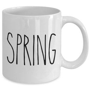 Puede incluir: Taza de cer&aacute;mica blanca con la palabra "SPRING" en letras negras manuscritas. La taza tiene un asa curvada y un acabado brillante. Un dise&ntilde;o sencillo para disfrutar de su bebida favorita.