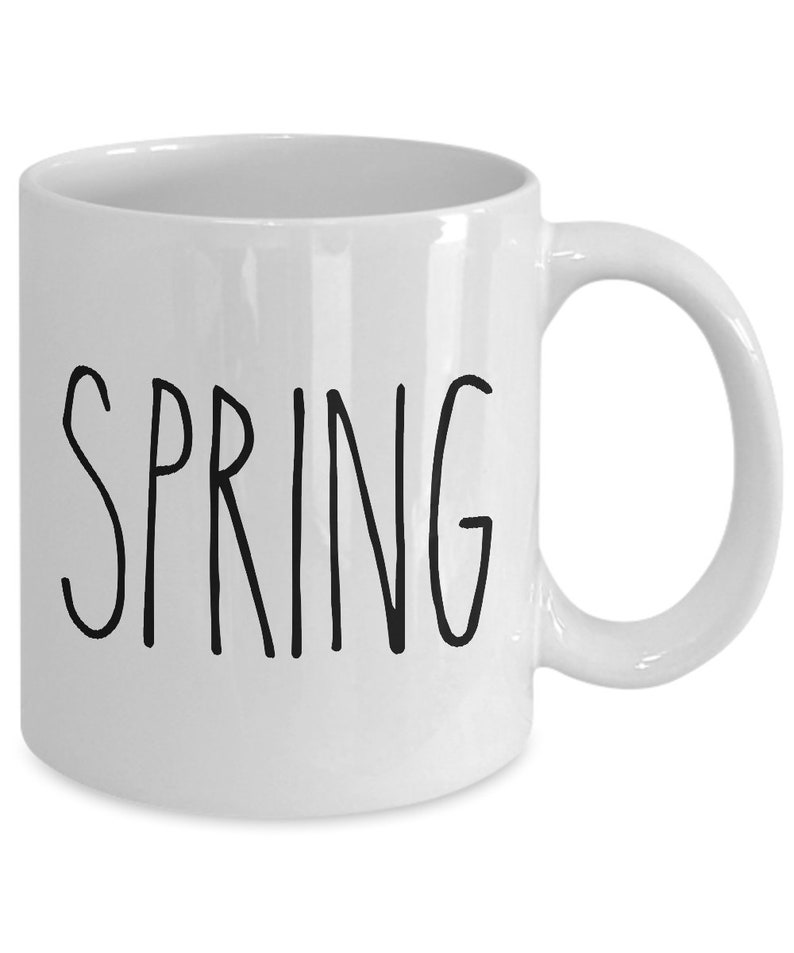 Puede incluir: Taza de cer&aacute;mica blanca con la palabra "SPRING" en letras negras manuscritas. La taza tiene un asa curvada y un acabado brillante. Un dise&ntilde;o sencillo para disfrutar de su bebida favorita.