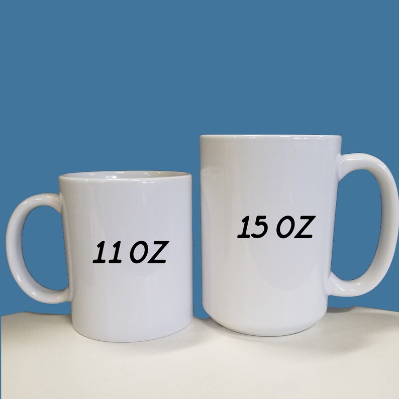 Puede incluir: Dos tazas de cer&aacute;mica blancas de diferentes tama&ntilde;os se muestran sobre un fondo azul. La taza m&aacute;s peque&ntilde;a est&aacute; etiquetada como "11 OZ" y la taza m&aacute;s grande como "15 OZ". Ambas tazas tienen un dise&ntilde;o sencillo con un asa curvada.