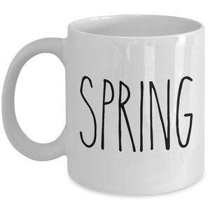 Puede incluir: Taza de cer&aacute;mica blanca con asa curva. La palabra "SPRING" est&aacute; impresa en negro, con letras manuscritas, en la parte delantera de la taza. La taza est&aacute; vac&iacute;a y sobre un fondo blanco.