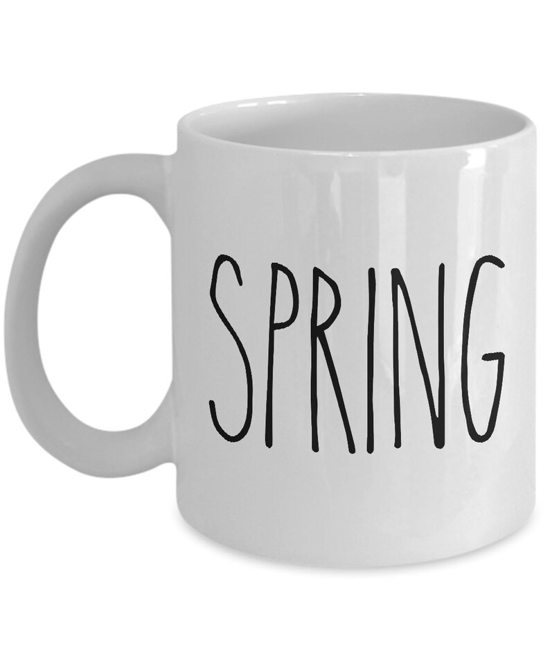 Puede incluir: Taza de cer&aacute;mica blanca con asa curva. La palabra "SPRING" est&aacute; impresa en negro, con letras manuscritas, en la parte delantera de la taza. La taza est&aacute; vac&iacute;a y sobre un fondo blanco.