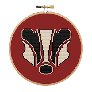 May include: A red cross-stitch embroidery hoop with a white and black badger face design.