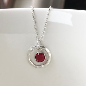 May include: A silver necklace with a hammered circle pendant featuring a red gemstone.