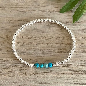 May include: A silver beaded bracelet featuring a row of turquoise beads. The bracelet is composed of small, round, silver beads. The turquoise beads are faceted, providing a contrast to the silver beads.