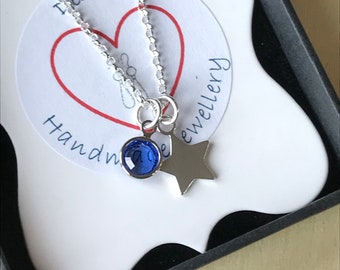 May include: A silver necklace with a blue crystal and a star charm. The necklace is in a black box with a white label that says "Destini Handmade Jewellery".
