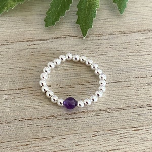 May include: A silver beaded ring with a single purple amethyst gemstone.