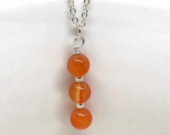 May include: A silver chain necklace with a pendant made of three orange carnelian beads.